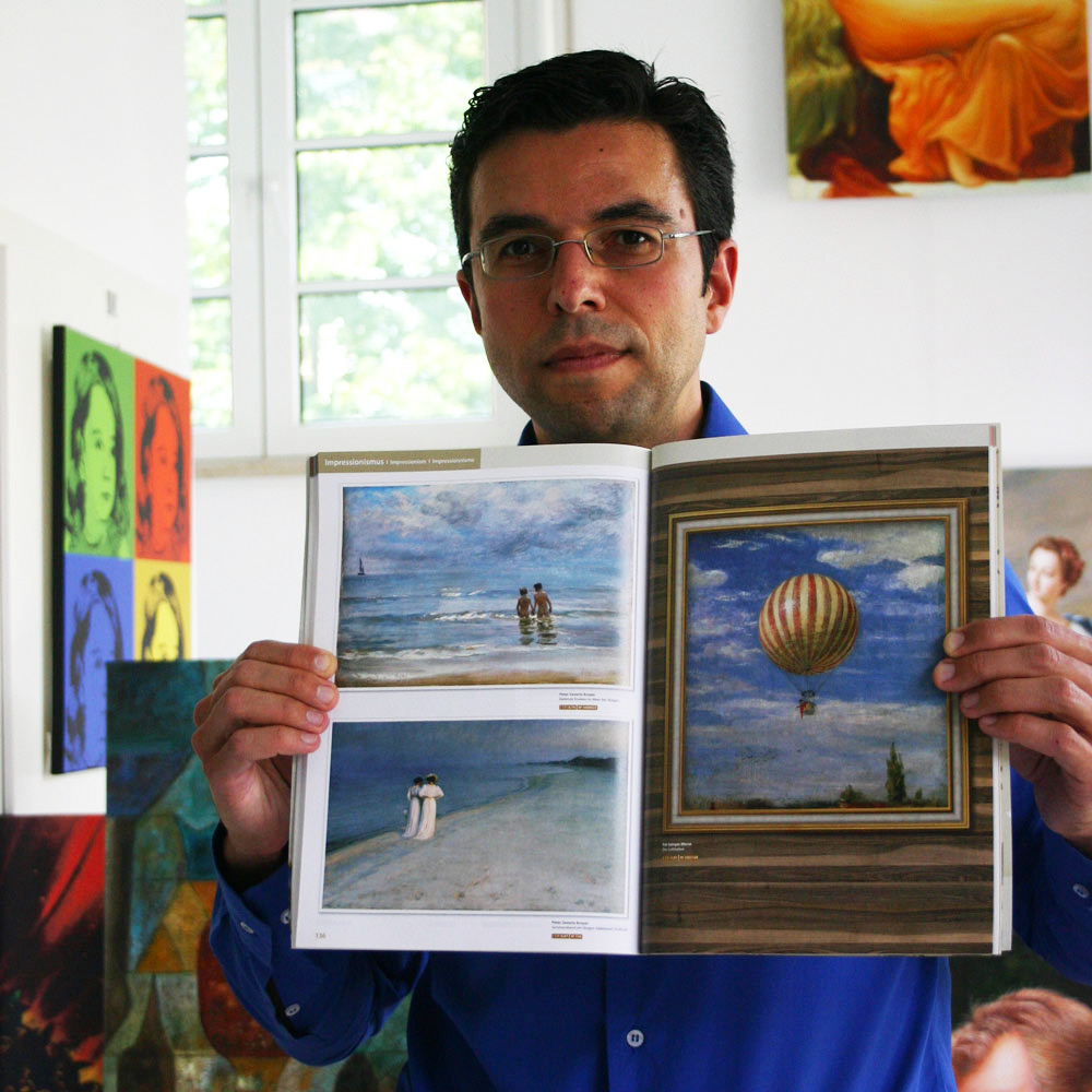 Inhaber Daniel Cid Gomez mit einem Kunstkatalog mit bestimmten Farben